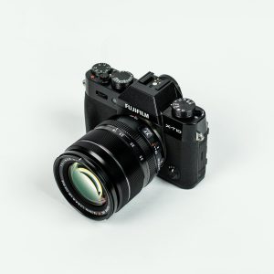 Close-up of a Fujifilm camera with lens on a plain background, showcasing photographic equipment.